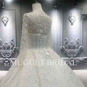 May include: A white wedding dress with long sleeves and a full skirt. The dress is covered in sequins and beads. The dress is being displayed on a mannequin in a store.