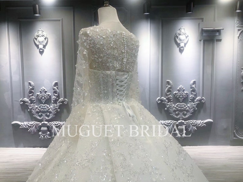 May include: A white wedding dress with long sleeves and a full skirt. The dress is covered in sequins and beads. The dress is being displayed on a mannequin in a store.