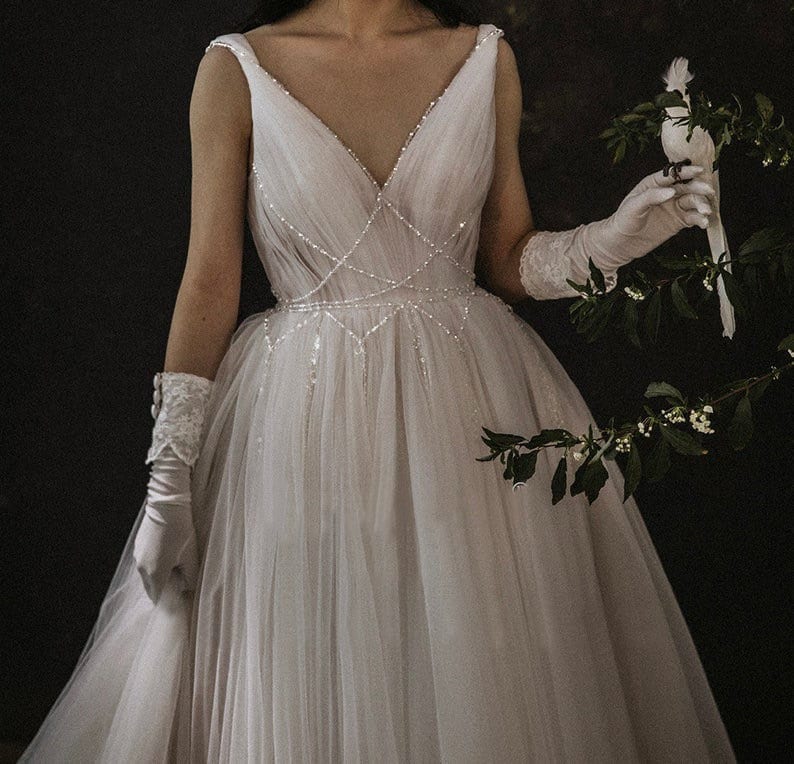 May include: A white tulle wedding dress with a V-neckline and a beaded bodice. The dress has a full skirt and is adorned with delicate beading.