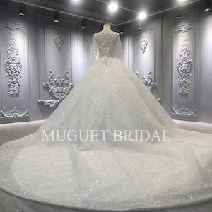 May include: A white wedding dress with a long train and a lace bodice. The dress is covered in sequins and has a fitted bodice with a sweetheart neckline. The dress is shown from the back and has a zipper closure.