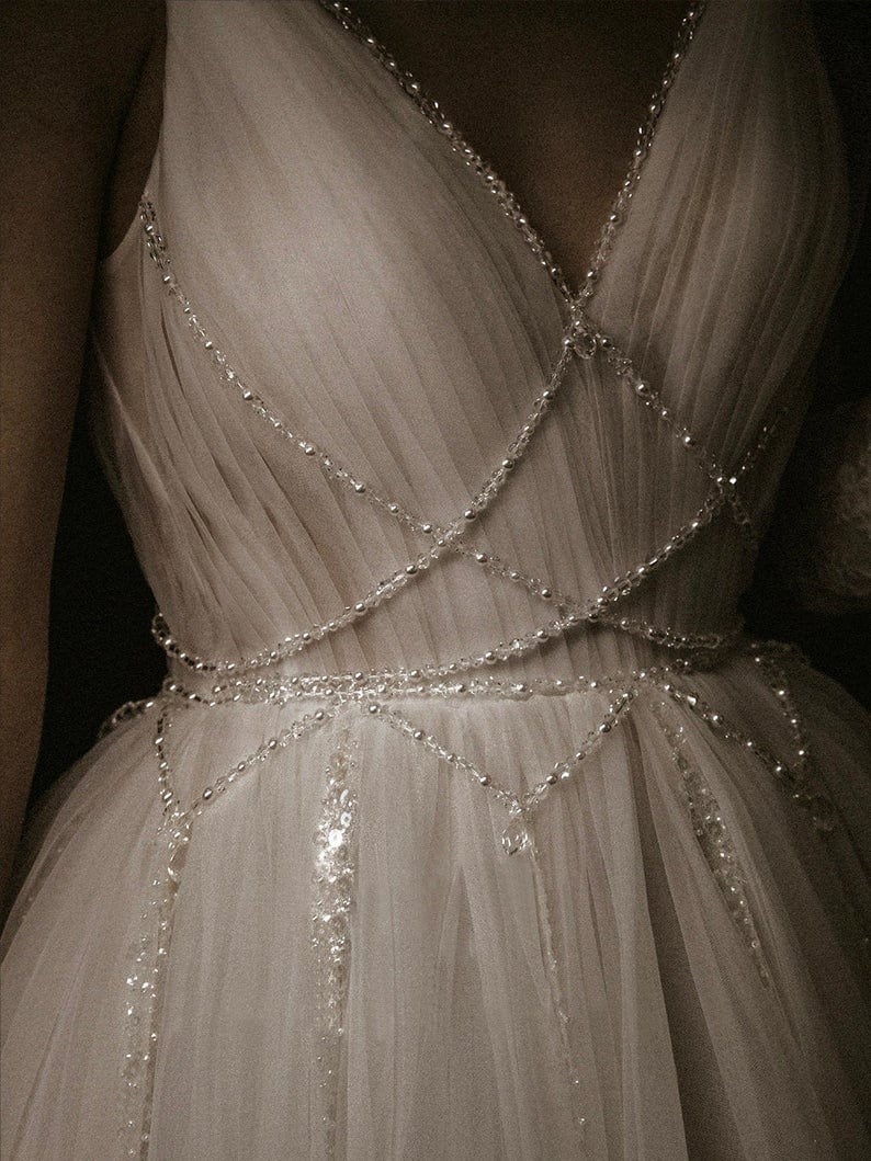 May include: A white tulle dress with a beaded bodice and a flowing skirt. The beads are arranged in a criss-cross pattern and create a delicate and elegant look.