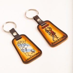 以下が含まれることがあります： 金属製のリングが付いた革製のキーホルダー2つ。1つのキーホルダーはアルゼンチンの地図と「アルゼンチン」の文字が書かれており、もう1つのキーホルダーはタンゴを踊るカップルと「タンゴアルゼンチン」の文字が書かれています。