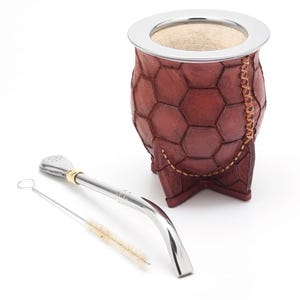 Puede incluir: Una calabaza mate de cuero marrón con una tapa de metal plateado y una bombilla de metal plateado con un cepillo para limpiar.