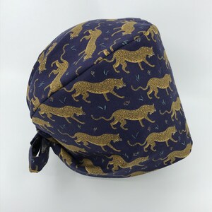 May include: A navy blue surgical scrub hat with a gold leopard print pattern.