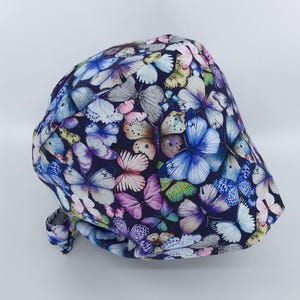 May include: A blue scrub hat with a colorful butterfly print. The hat is made of a soft, comfortable fabric and has a tie at the back.
