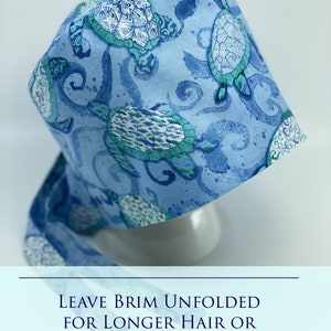 May include: A blue surgical cap with a pattern of sea turtles and swirls. The text "LEAVE BRIM UNFOLDED FOR LONGER HAIR OR LOOSER FIT" is printed on the bottom of the image.