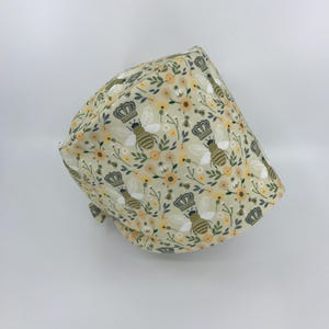 May include: A light green scrub hat with a pattern of bees, flowers, and crowns.