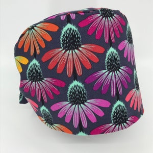 May include: A dark gray fabric scrub hat with a colorful floral print featuring pink, red, orange, and green flowers. The flowers have a black center and are arranged in a repeating pattern.