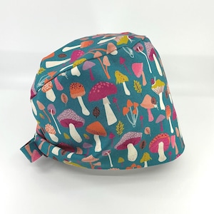 May include: A teal scrub cap featuring a repeating pattern of various mushrooms in shades of pink, orange, yellow, and white. The fabric displays diverse fungi shapes, including spotted caps and slender stems, distributed across the entire surface.