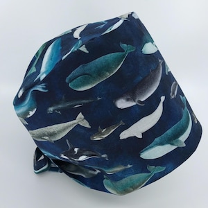 May include: A blue scrub hat with a whale print. The hat features a variety of whales in different sizes and colors, including blue, gray, and white. The hat is made of a soft, comfortable fabric and is perfect for nurses, doctors, and other healthcare professionals.