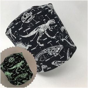 May include: Black fabric hat featuring a white dinosaur skeleton design with labeled bone structures. The hat includes a smaller, glowing version of the same design. The text includes anatomical terms like "Pelvis" and "Phalanx".