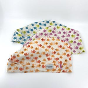 May include: Three patterned scrub caps. One cap has a white background with orange and yellow fish. Another has a white background with purple fish. The third cap has a white background with blue and green fish. The caps have a tag that says "Hudson Bonus Care".