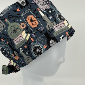 May include: A dark teal surgical scrub cap with a repeating pattern of potion bottles, spiders, books, and botanical elements. The cap features the text "Age of Sorcery" and "500 Ancient Beasts".