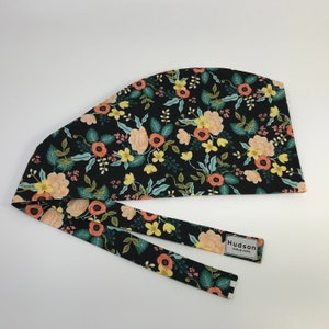 May include: Black scrub cap with a floral pattern in peach, yellow, and teal. The cap has a tie-back design and a label that reads "Hudson Scrub Caps."