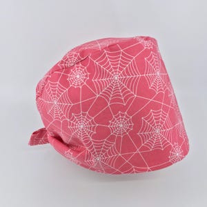 May include: Pink surgical scrub hat with a white spiderweb pattern.