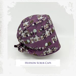 May include: A purple scrub cap with a Halloween-themed pattern featuring potion bottles, spiderwebs, and jack-o'-lanterns. The cap has a curved design and a tie in the back. The text "HUDSON SCRUB CAPS" is at the bottom.