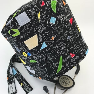 May include: Black scrub cap with a white print of mathematical equations, formulas, and symbols. The cap has a tie on the back and a small tag that says "Hudson Scrub Caps".