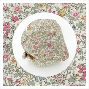 May include: A floral print hat featuring pink, yellow, and white flowers with cartoon animal figures on a light green background. The hat has a rounded crown and a tied back.