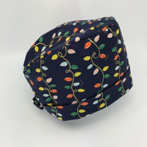 May include: A navy blue scrub hat with a pattern of colorful Christmas lights. The hat has a tie on the back.