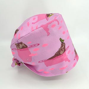 May include: Pink surgical scrub hat with a pattern of hippos in a pink pond with pink fish and a butterfly on one hippo's head.