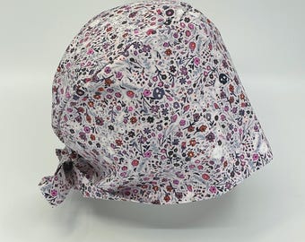 May include: A floral patterned cap featuring a mix of small flowers and skull designs in shades of pink, purple, and black on a white background. The cap is tied at the back with a matching fabric tie.