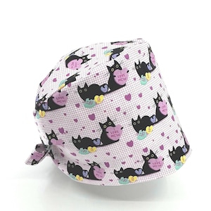 May include: A white and pink patterned surgical scrub cap featuring black cat illustrations holding heart-shaped candies. The candies have the text "FUR YOU" and "LOVE MEW". The cap also has purple hearts and the text "LOVE MEW".