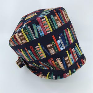 May include: A dark blue scrub hat with a pattern of colorful books. The books have titles like "Gulliver's Travels", "Heidi", and "The Jungle Book".