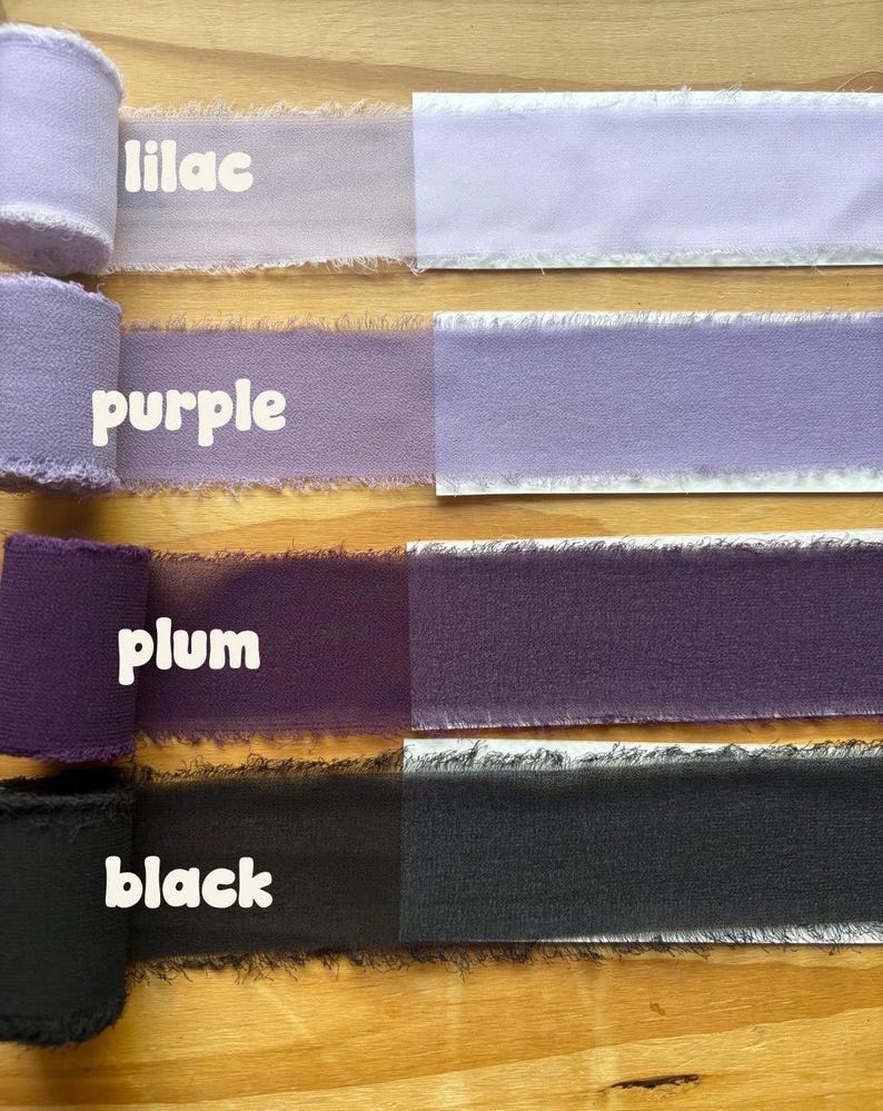 May include: A selection of fabric ribbons in various shades of purple and black, including lilac, purple, plum, and black. Each ribbon is labeled with its color name in white text. The ribbons have a frayed edge and are displayed on a wooden surface.