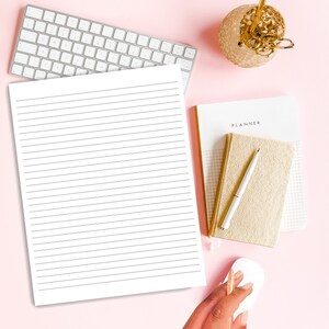 May include: A white lined notebook with a gold planner and pen on a pink surface. The planner has the word "PLANNER" printed on the front.