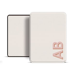 May include: A pair of off-white rectangular notebooks with rounded corners. One notebook is open, revealing a textured interior. The cover of the other notebook features the embossed letters "AB" in a copper color.