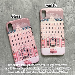 May include: Two phone cases, one glossy and one matte, featuring a pink building design with the text "GRAND BUDAPEST HOTEL". The matte case is lighter in color. A pink truck is visible on the bottom of the cases.