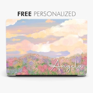 Könnte beinhalten: Eine Laptop-Haut mit einem pastellfarbenen Sonnenuntergangshimmel und einem Blumenfeld. Der Name "Angela" ist in Kursivschrift in der unteren rechten Ecke der Haut geschrieben.