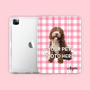 May include: A clear tablet case and a folding cover featuring a pink and white gingham pattern. The cover displays a brown curly-haired dog, the text "YOUR PET PHOTO HERE" with two paw prints, and the name "Angela" in a black script font.