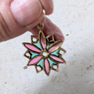 May include: A gold-toned earring with a floral design. The flower has pink and light blue petals, with a gold outline. The earring is held up by a small hook.