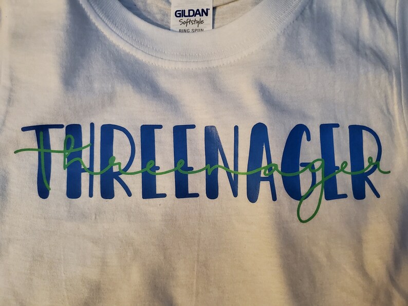 May include: White t-shirt with the text "THREEnager" in blue and green lettering.