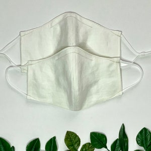May include: Two white cotton face masks with elastic ear loops. The masks are stacked on top of each other.