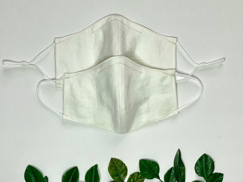 May include: Two white cotton face masks with elastic ear loops. The masks are stacked on top of each other.