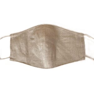May include: A beige face mask made of textured fabric. The mask has white elastic ear loops and is designed to cover the nose and mouth. The mask is a neutral color and appears to be made of a breathable material.