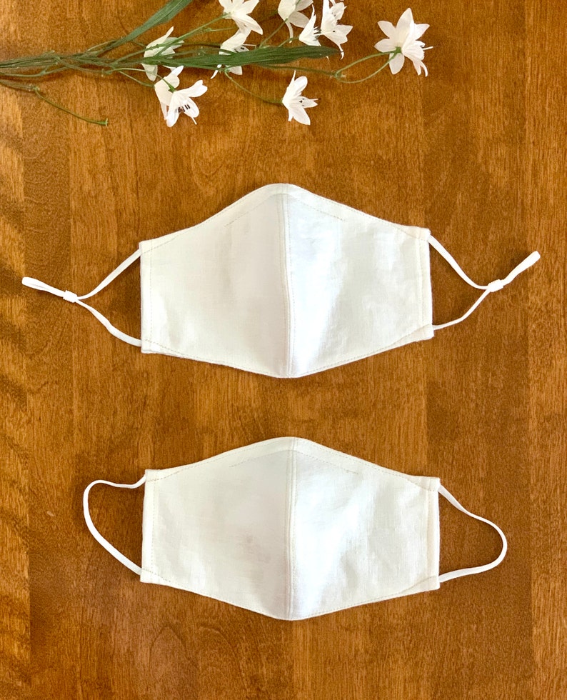 May include: Two white cotton face masks with elastic ear loops. The masks are plain and have a simple design.
