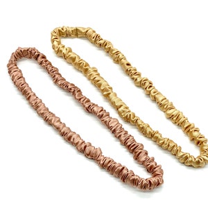 May include: Two hair scrunchies made of silky fabric. One is a light brown color and the other is a gold color.