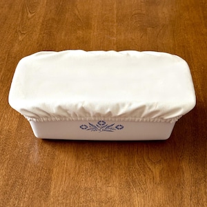 May include: White cotton bread loaf cover with a blue and white floral design on a wooden surface.