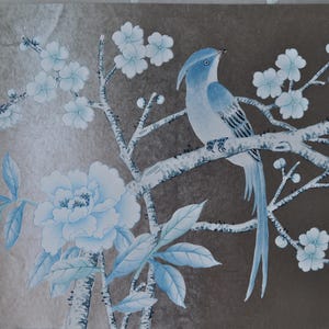 Könnte beinhalten: Detaillierte Illustration eines blauen Vogels, der auf einem Ast mit weißen Blüten und Blättern sitzt. Der Vogel hat einen langen Schwanz und ist vor einem braunen Hintergrund platziert. Das Kunstwerk zeigt eine große Blume.