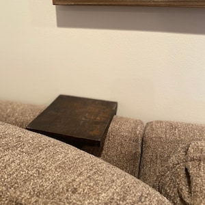 Puede incluir: Una mesa auxiliar de madera marrón oscuro con una tapa rectangular se encuentra sobre un sofá marrón.