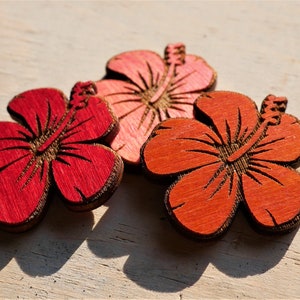 May include: Three wooden hibiscus flowers in shades of red, orange, and pink. The flowers are carved with intricate details and have a rustic, natural look.