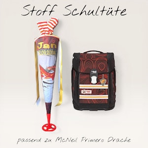 Könnte beinhalten: Ein Schulranzen- und Schultüten-Set. Die Schultüte ist weiß, blau und rot mit einer Drachenillustration und dem Namen "Jan" und dem Datum "09.09.2024". Der Rucksack ist schwarz und rot mit einem einzigartigen Muster.