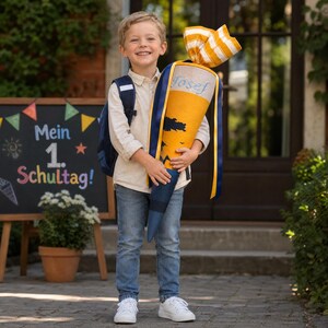Könnte beinhalten: Ein lächelnder Junge hält eine große gelb-blaue Schultüte mit dem Namen "Josef". Die Tüte ist mit einer schwarzen Silhouette verziert und hat einen gestreiften oberen Teil. Eine Tafel im Hintergrund zeigt den Text "Mein 1. Schultag!"
