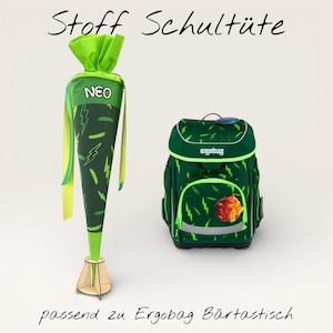 Könnte beinhalten: Ein grüner und gelber Schulkegel und ein passender grüner Rucksack. Der Kegel ist mit Blitz- und Pinselstrich-Designs verziert. Der Rucksack hat ein ähnliches Muster und das Wort "ergobag". Der Text "Stoff Schultüte" steht oben.