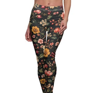 May include: Full-length leggings featuring a dark black background with a vibrant botanical print. The pattern includes various flowers in shades of yellow, orange, pink, and white, interspersed with green leaves and small berries.