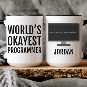 May include: Two white ceramic mugs with black handles and rims. One mug reads "WORLD'S OKAYEST PROGRAMMER" in black text. The other mug features a computer screen graphic and the name "JORDAN".