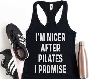 May include: Black tank top with the text "I'm nicer after Pilates I promise" in white lettering. The tank top is laying flat on a white background with a water bottle and two black sneakers.